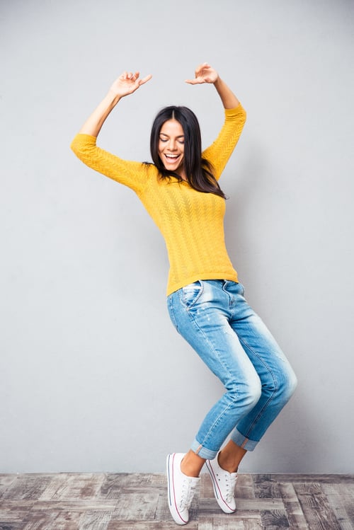 Portrait of a happy young woman dancing on gray background